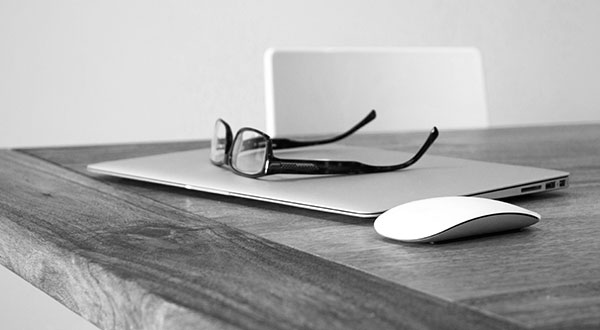 Computer portatile, occhiali e mouse su una scrivania